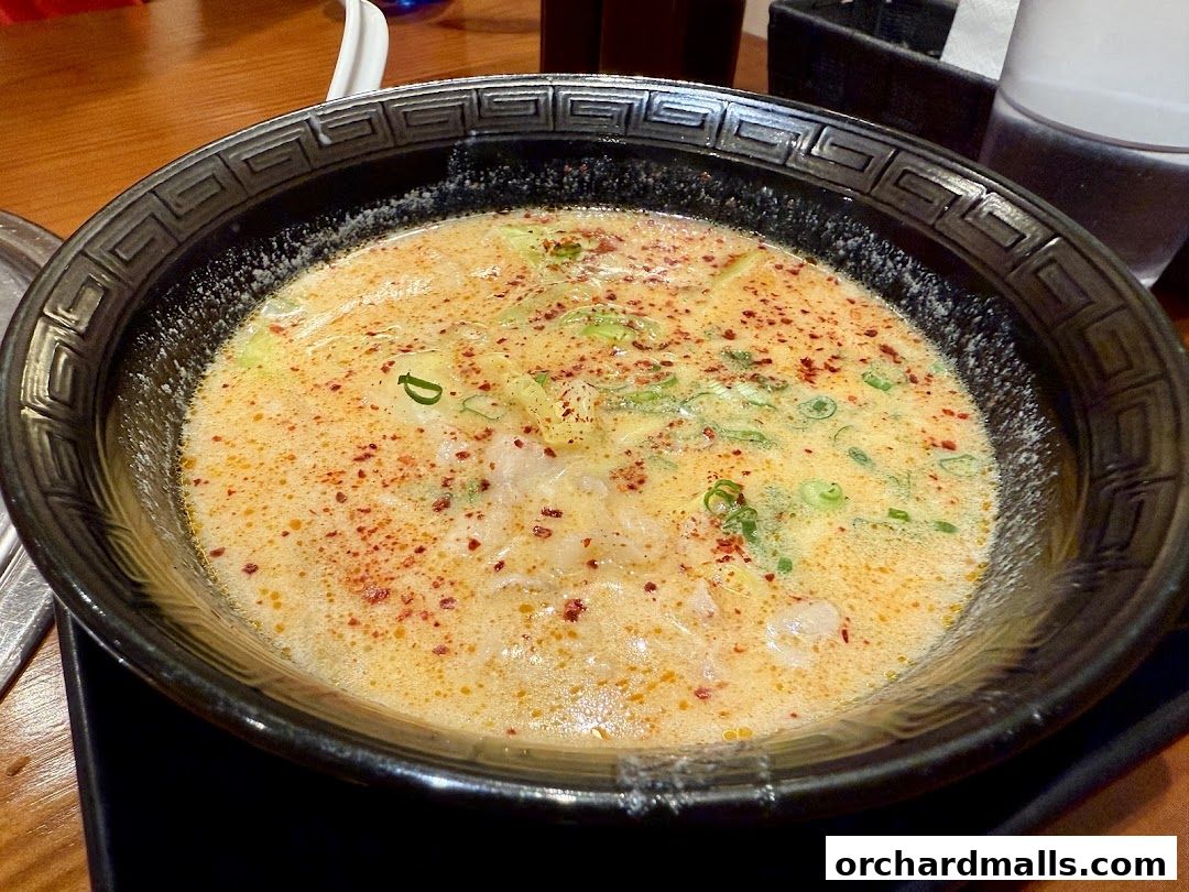 A close-up shot of a steaming bowl of ramen with a rich, creamy broth and green onions.