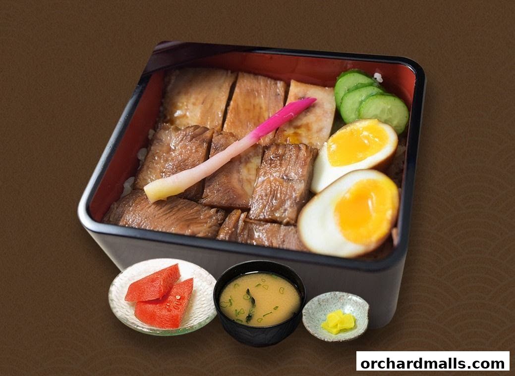 A bento box with grilled meat, rice, egg, cucumber, pickled ginger, miso soup, and pickled radish.
