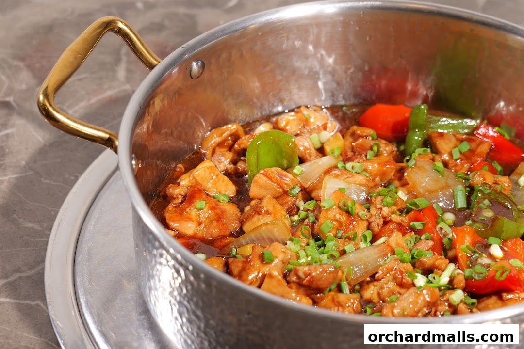 A close-up of a pot filled with savory chicken, peppers, and onions, garnished with green onions.