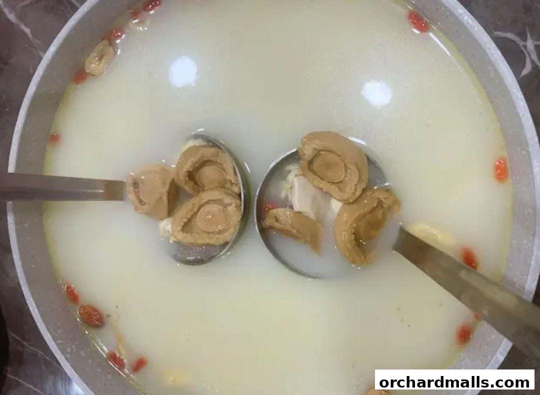 A close-up of a pot of soup with abalone and goji berries, being served with ladles.