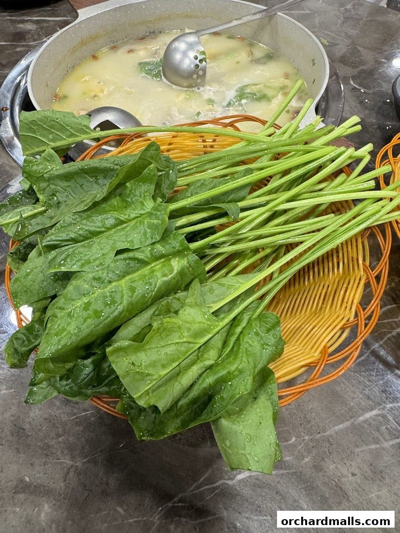 A basket of fresh green vegetables sits in front of a pot of simmering soup.