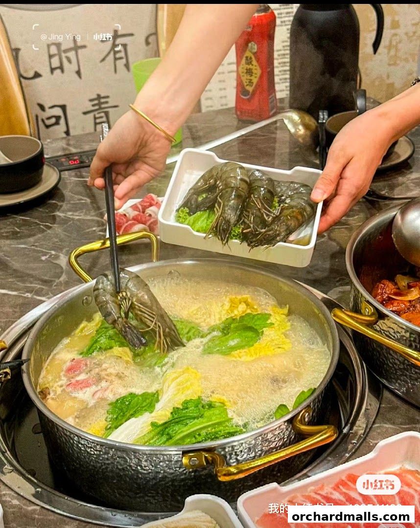 A person is adding a large shrimp to a bubbling hot pot with vegetables and meat.