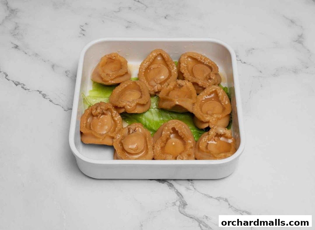 A white square dish filled with braised abalone on a bed of lettuce.