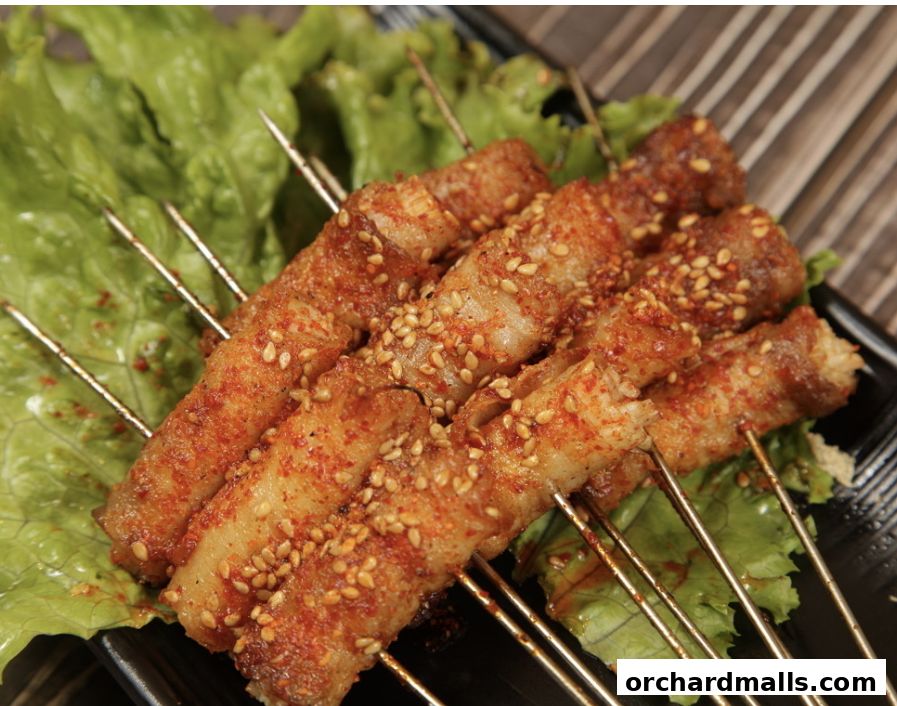 Close-up of grilled pork belly skewers seasoned with chili and sesame seeds on lettuce.