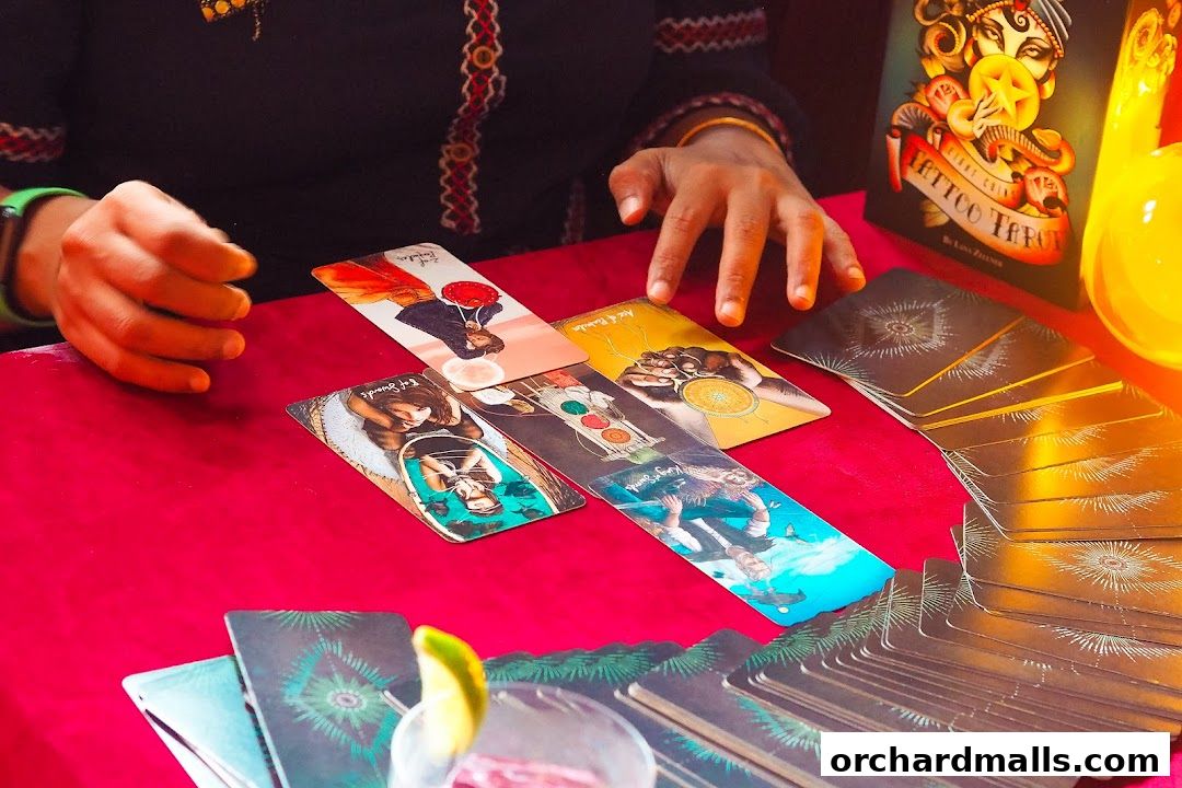 A person's hands are shown over a spread of tarot cards on a red cloth.