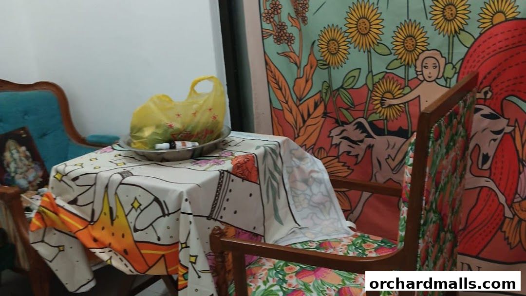 A table with a patterned cloth, a yellow bag, and chairs with vibrant floral upholstery.