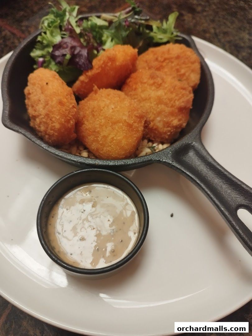Crispy fried bites served in a cast iron skillet with a side of dipping sauce and salad.