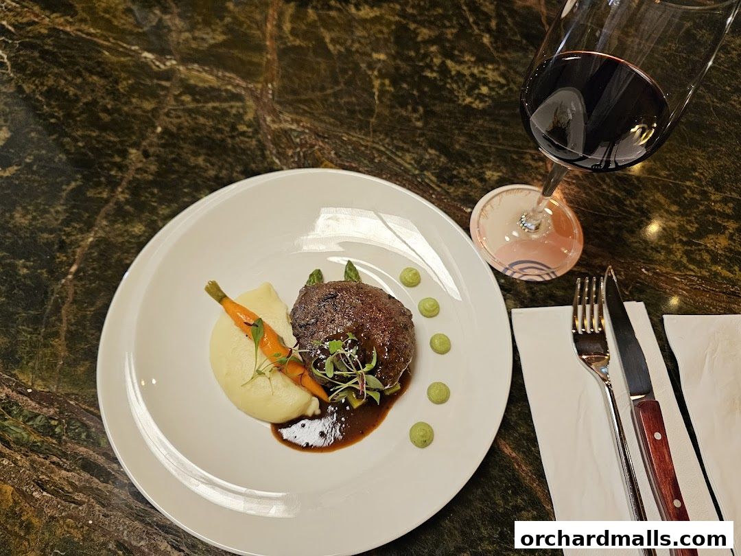 A gourmet dish of meat, mashed potatoes, and carrots served with a glass of red wine.