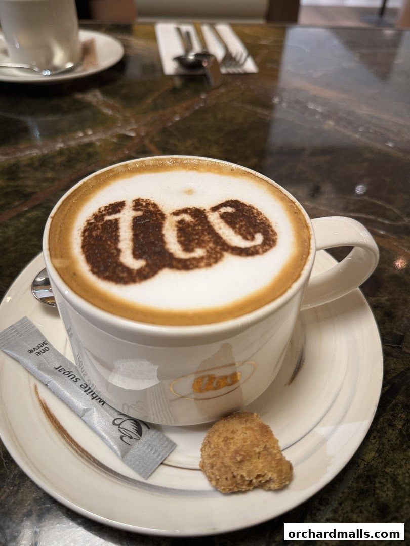 A cup of cappuccino with 'tcc' logo on foam, served with sugar and a cookie.
