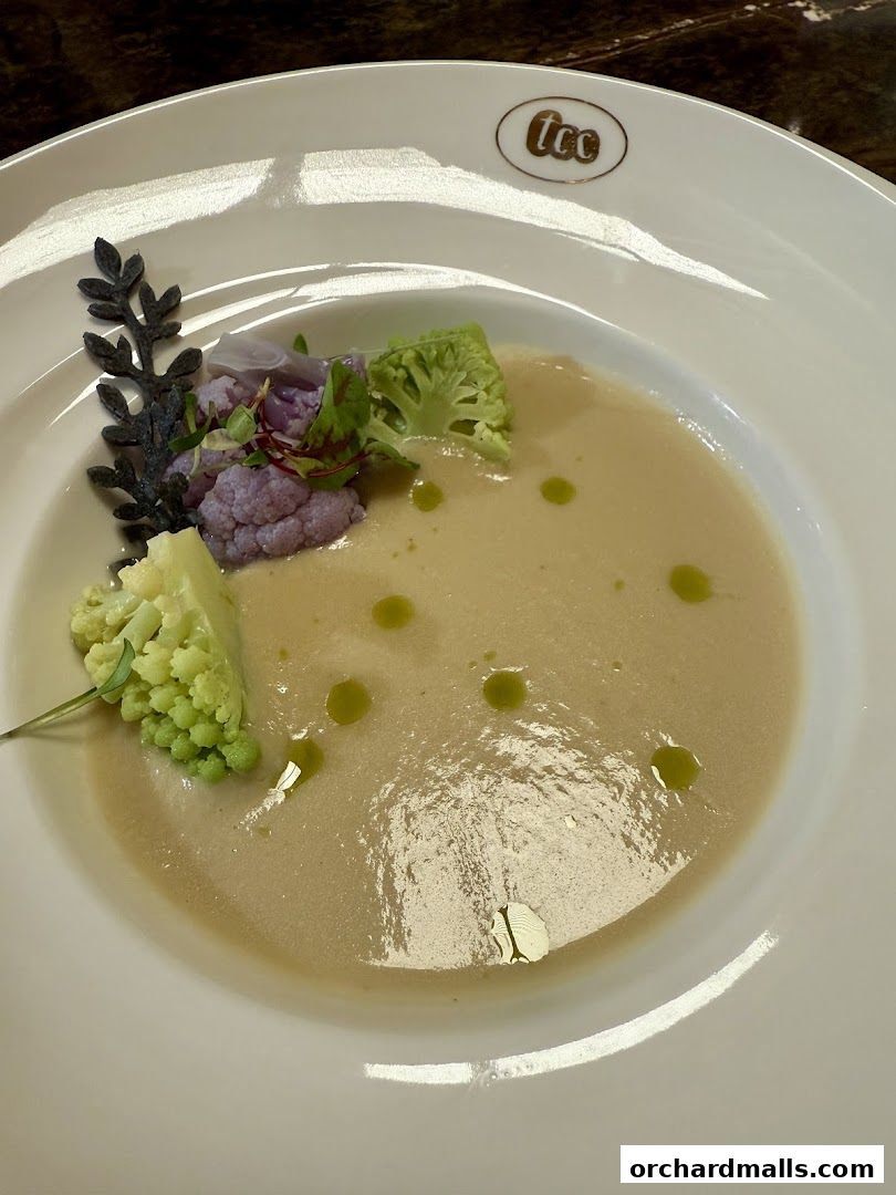 A creamy soup served in a white bowl with cauliflower and herbs.