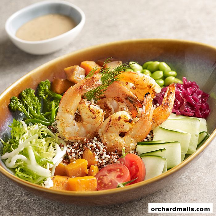 A vibrant shrimp and quinoa bowl with fresh vegetables and a side of dressing.