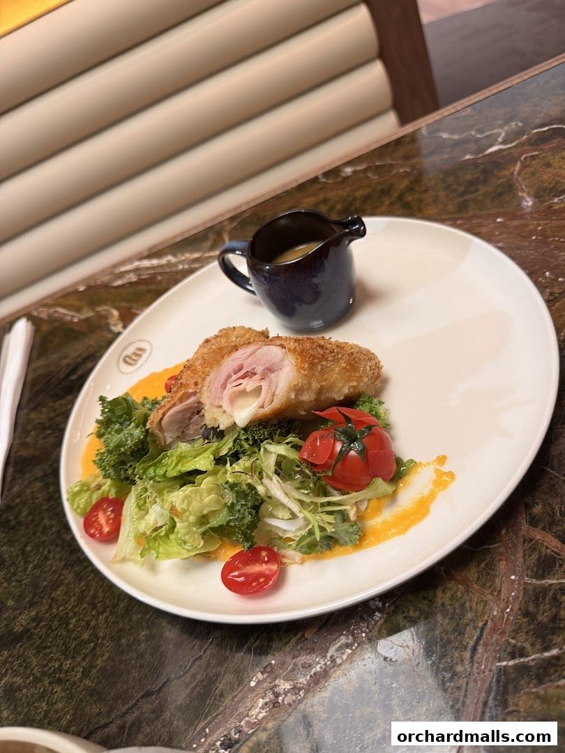A gourmet dish featuring breaded chicken stuffed with ham and cheese, served with salad and sauce.