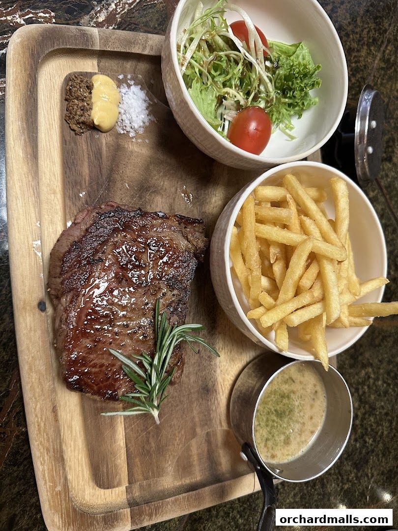 A perfectly grilled steak served with fries, salad, and a side of sauce on a wooden board.