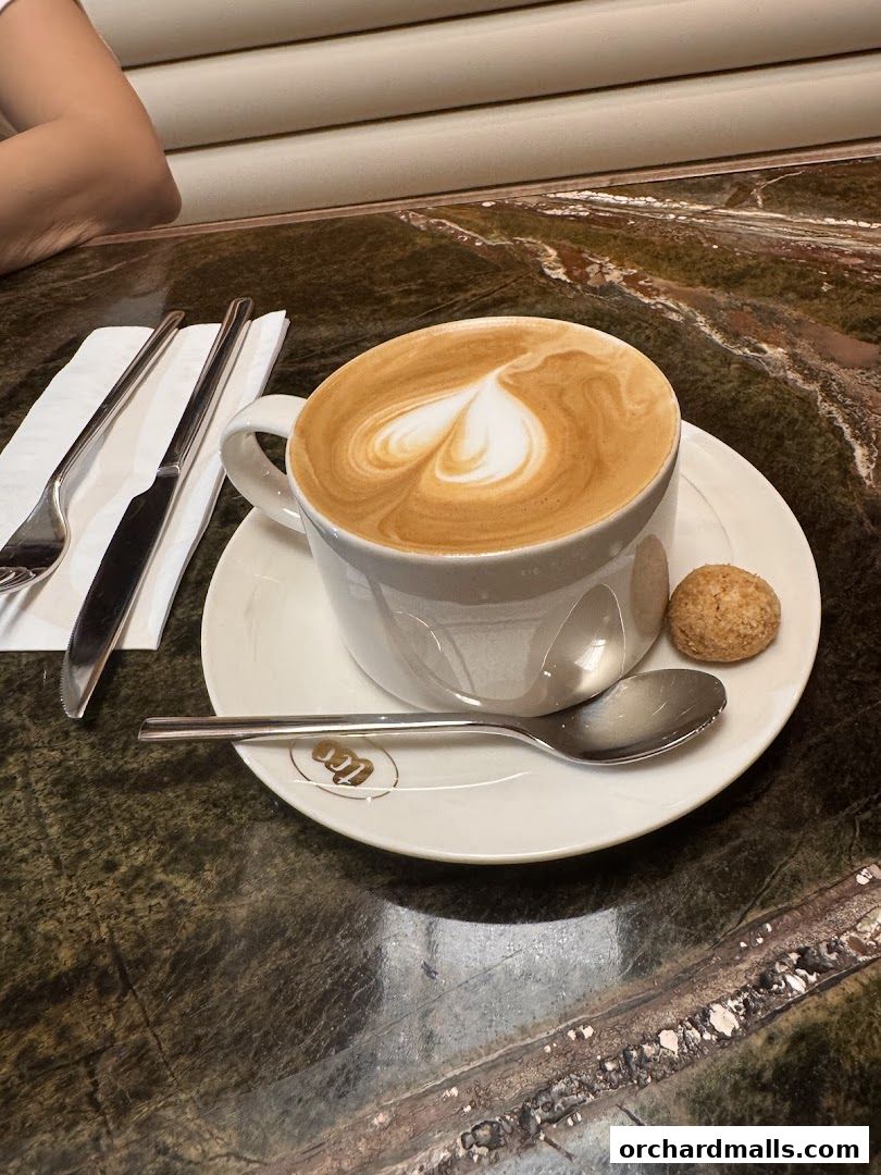 A beautifully crafted latte with heart art, served with a cookie and cutlery.