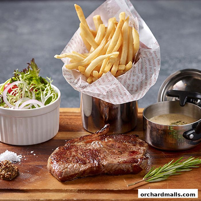 A juicy steak with french fries, salad, and sauce on a wooden board.