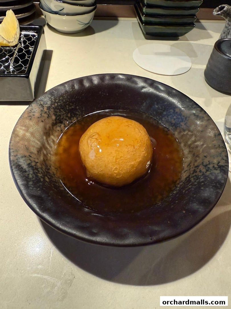 A close-up of a golden-brown sphere in a dark bowl filled with savory broth.