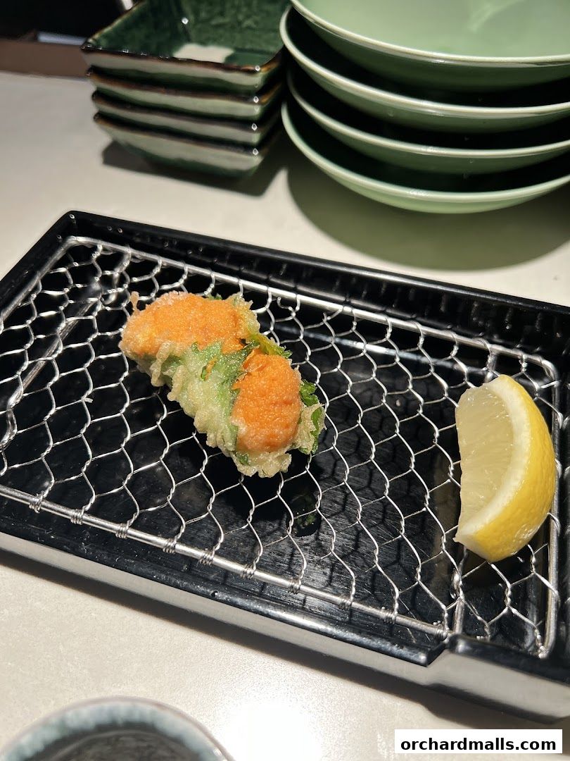 A close-up of tempura served on a wire rack with a lemon wedge.