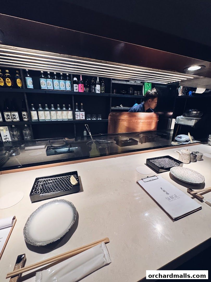 Interior view of a tempura restaurant counter with bottles and a chef in the background.