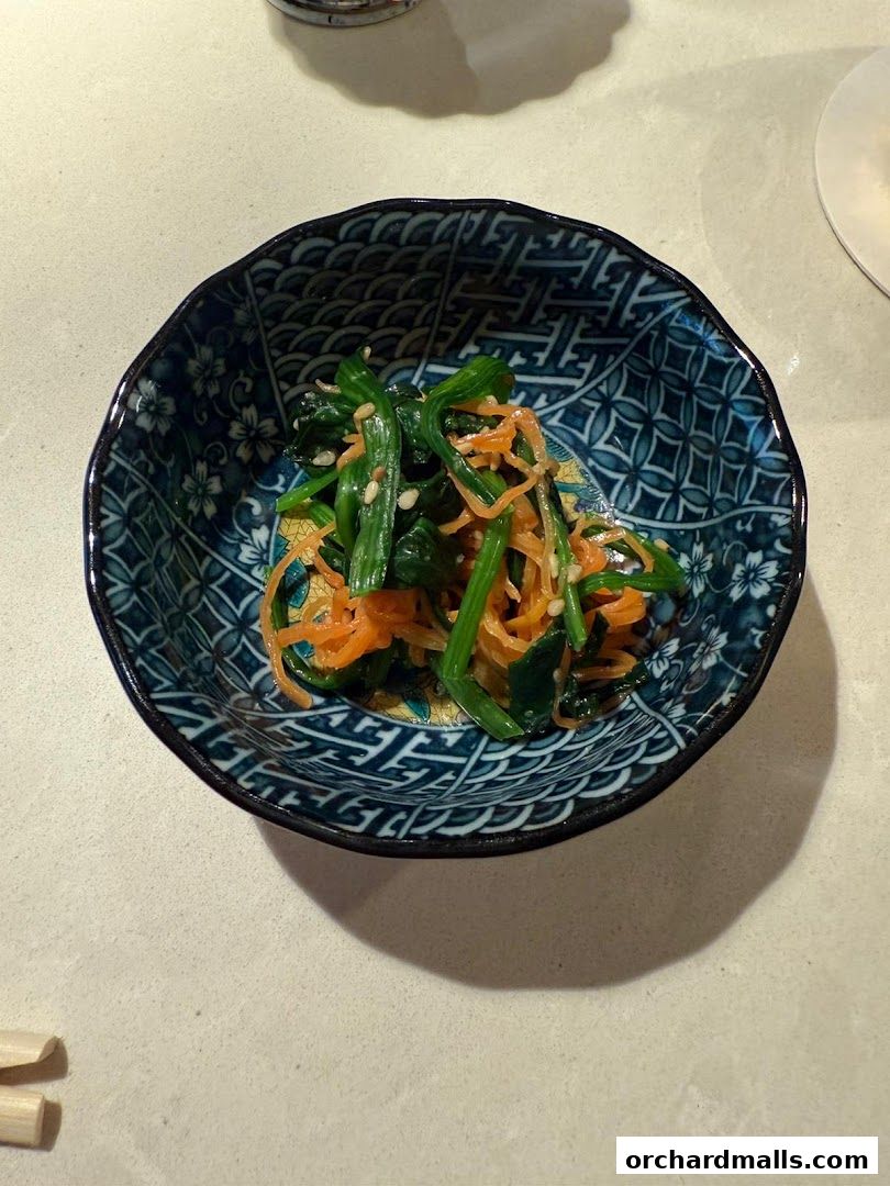 A decorative bowl filled with a fresh spinach and carrot salad.