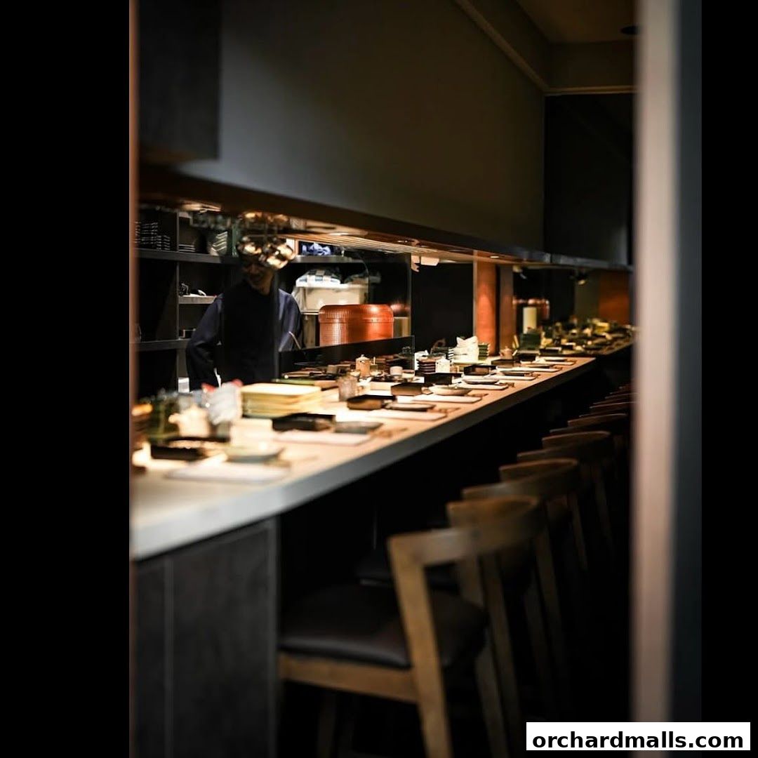 A chef stands behind a sushi bar with seating and prepared dishes.