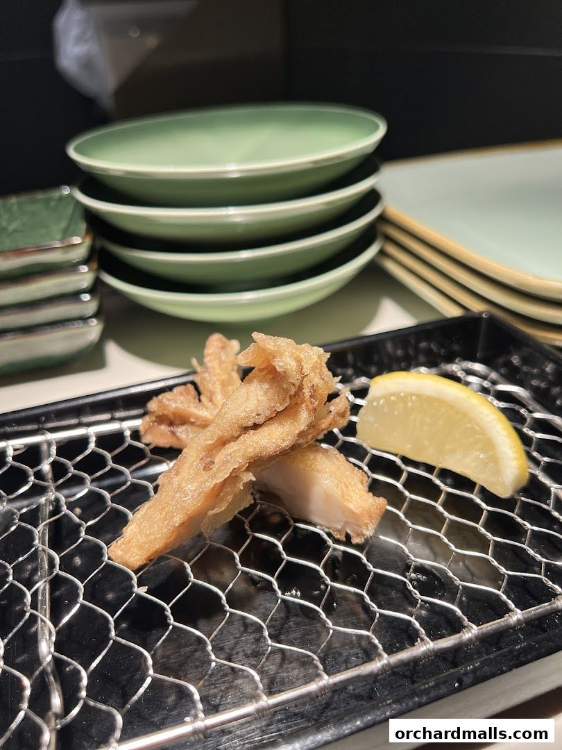 Crispy tempura served with a lemon wedge on a wire rack, with stacked plates in the background.
