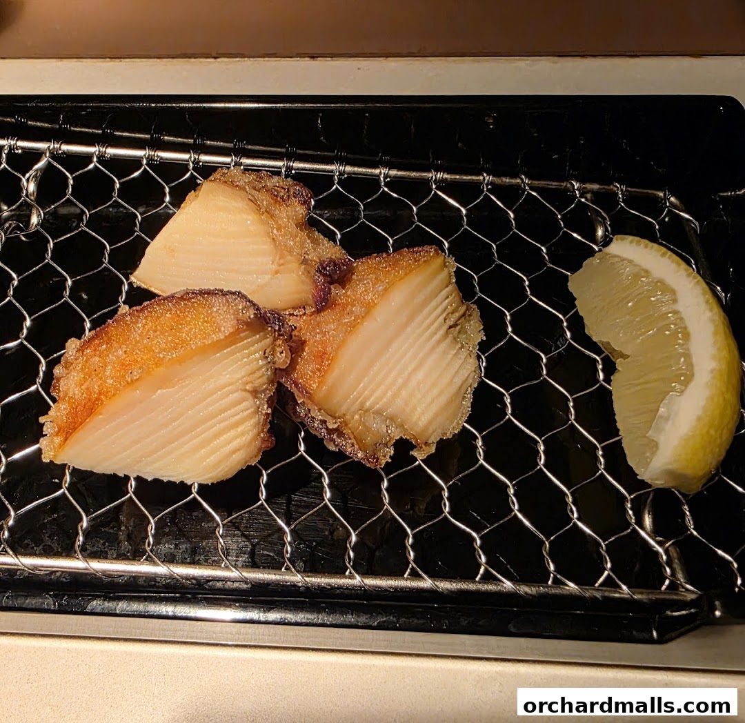 Three pieces of golden-brown tempura served with a lemon slice on a wire rack.