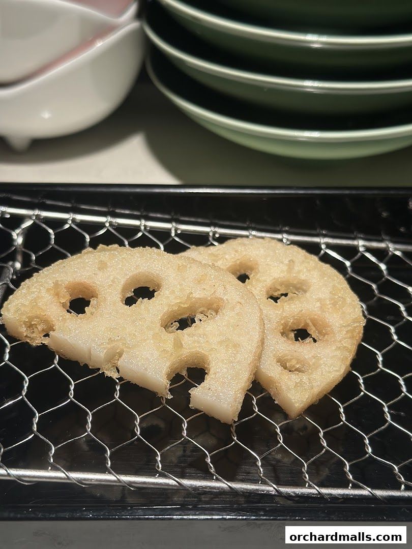 Two slices of crispy fried lotus root served on a wire rack.