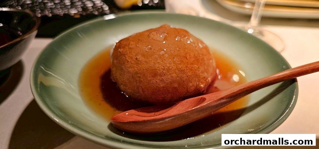 A close-up of a golden-brown tempura item in a light green bowl with broth and a wooden spoon.