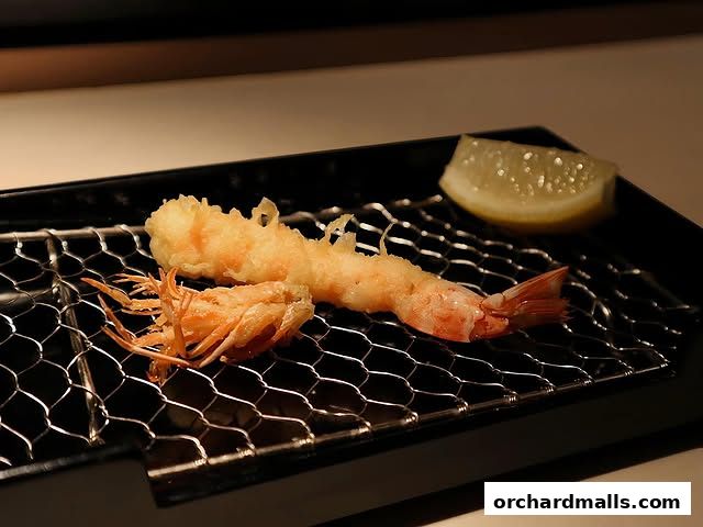 Crispy tempura shrimp and a lemon slice served on a wire rack.
