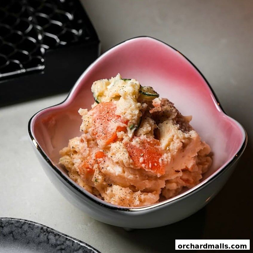 A close-up of a creamy potato salad with visible chunks of vegetables in a pink-rimmed bowl.