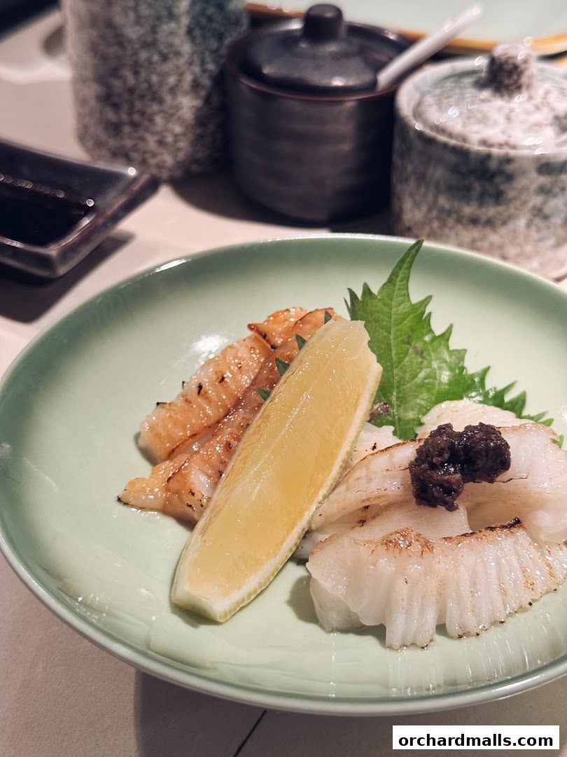 A light green plate holds grilled seafood with a lemon wedge and garnish.