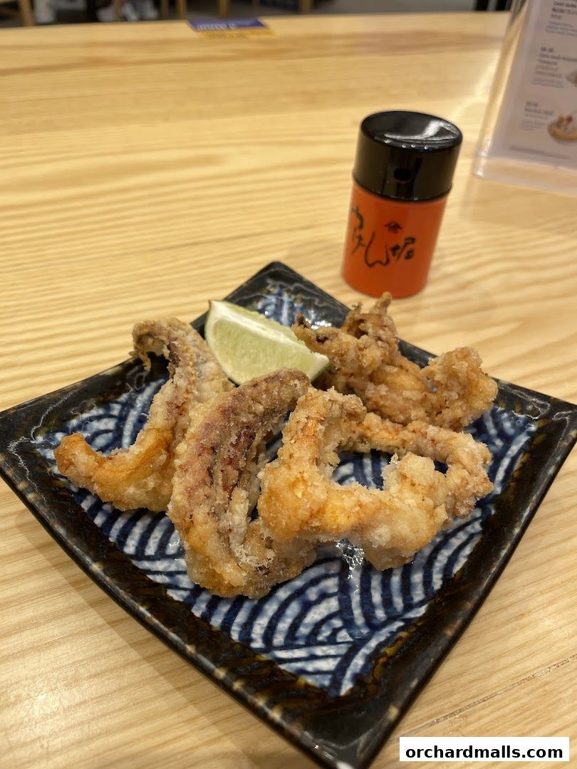 A plate of crispy fried calamari with a lime wedge and a small spice shaker.