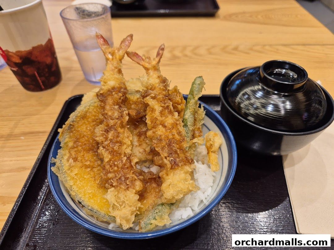 A close-up of a delicious tempura donburi with shrimp and vegetables served with rice and a side of soup.