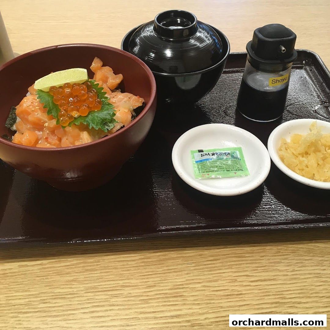 A bowl of salmon donburi with ikura, lime, and a side of tempura bits and soup.
