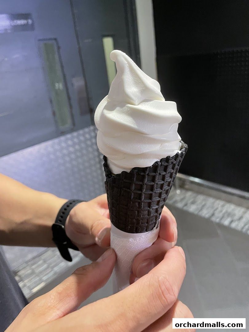 A person holds a white soft-serve ice cream cone with a black waffle cone.