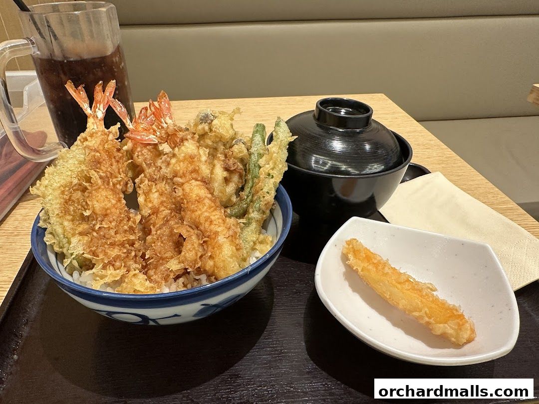 A bowl of tempura with rice, a side dish, and a drink.