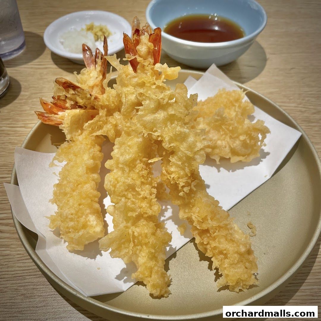 A close-up shot of crispy, golden-brown tempura shrimp served with dipping sauce and grated radish.