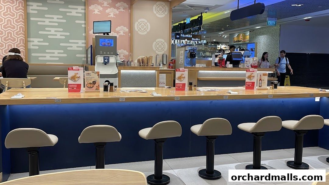 Interior view of a Japanese restaurant counter with bar stools and food displays.