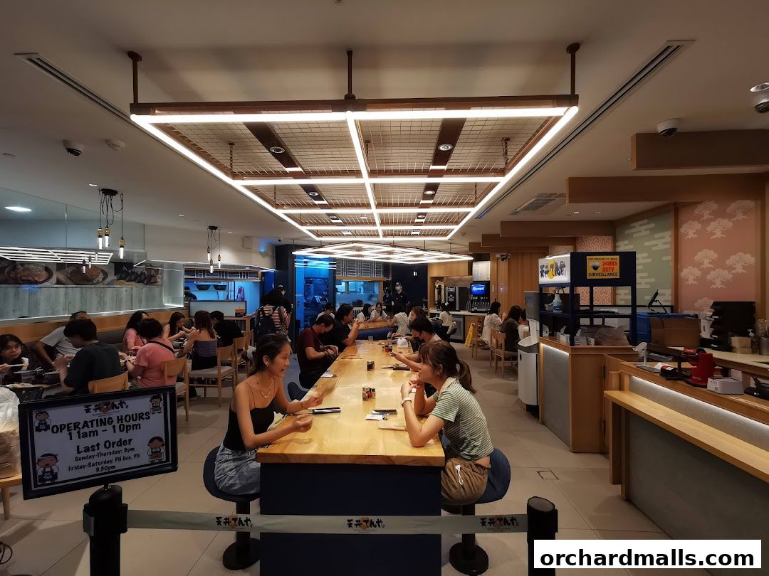 Interior of a busy Japanese restaurant with diners seated at a long communal table.