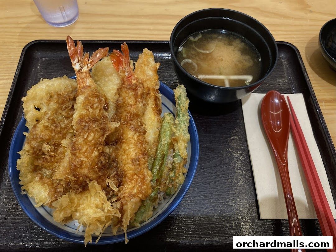 A bowl of tempura with shrimp and vegetables served with miso soup and chopsticks.