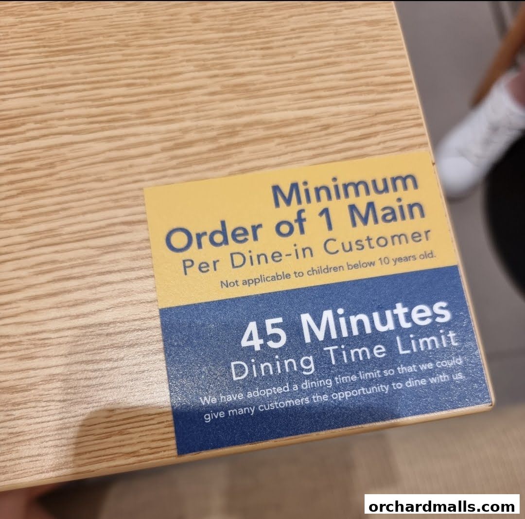A sticker on a wooden surface indicating a minimum order and dining time limit.
