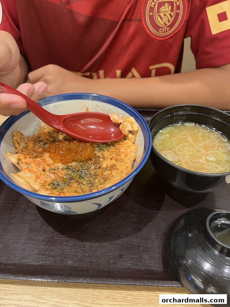 A person is eating a bowl of salmon donburi with a side of miso soup.