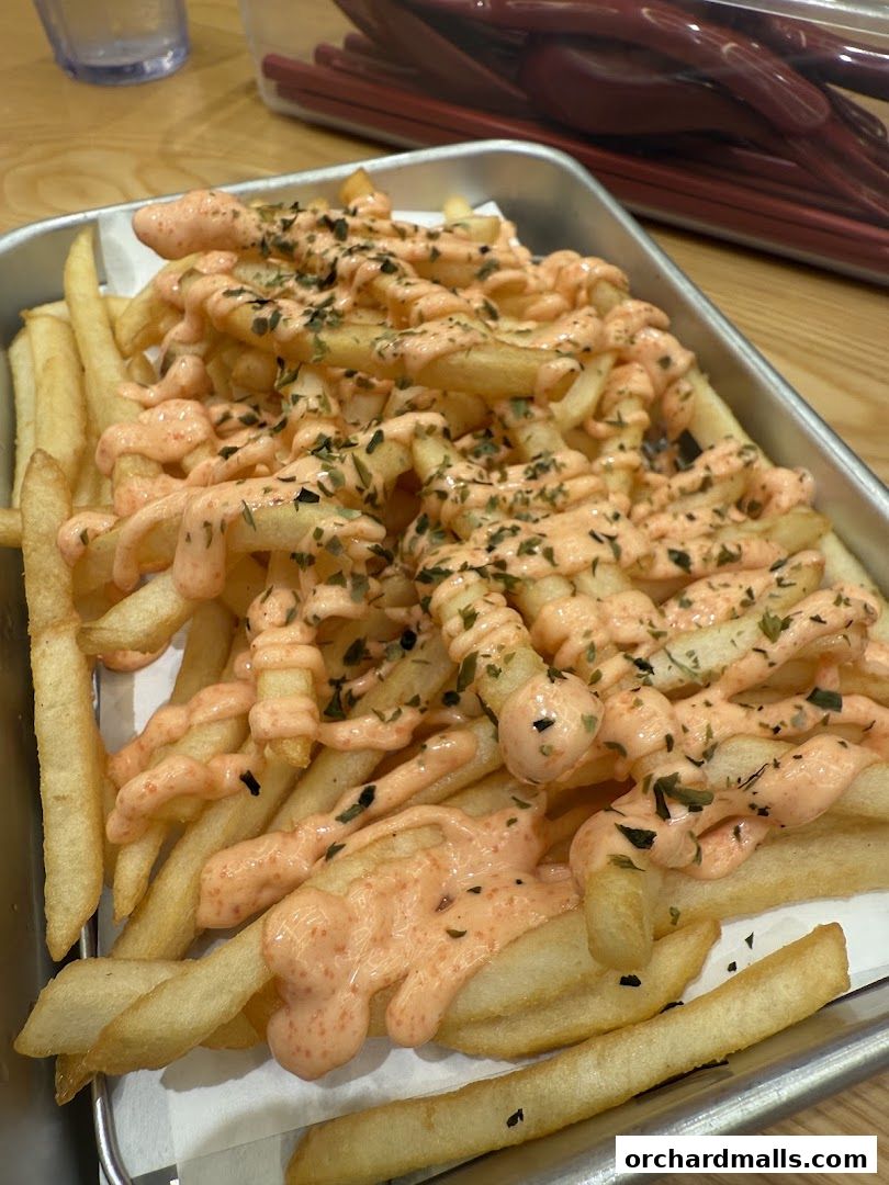 A close-up shot of crispy french fries topped with a creamy sauce and herbs.