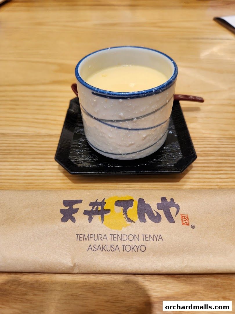 A close-up of a creamy dessert served in a patterned cup on a black saucer.