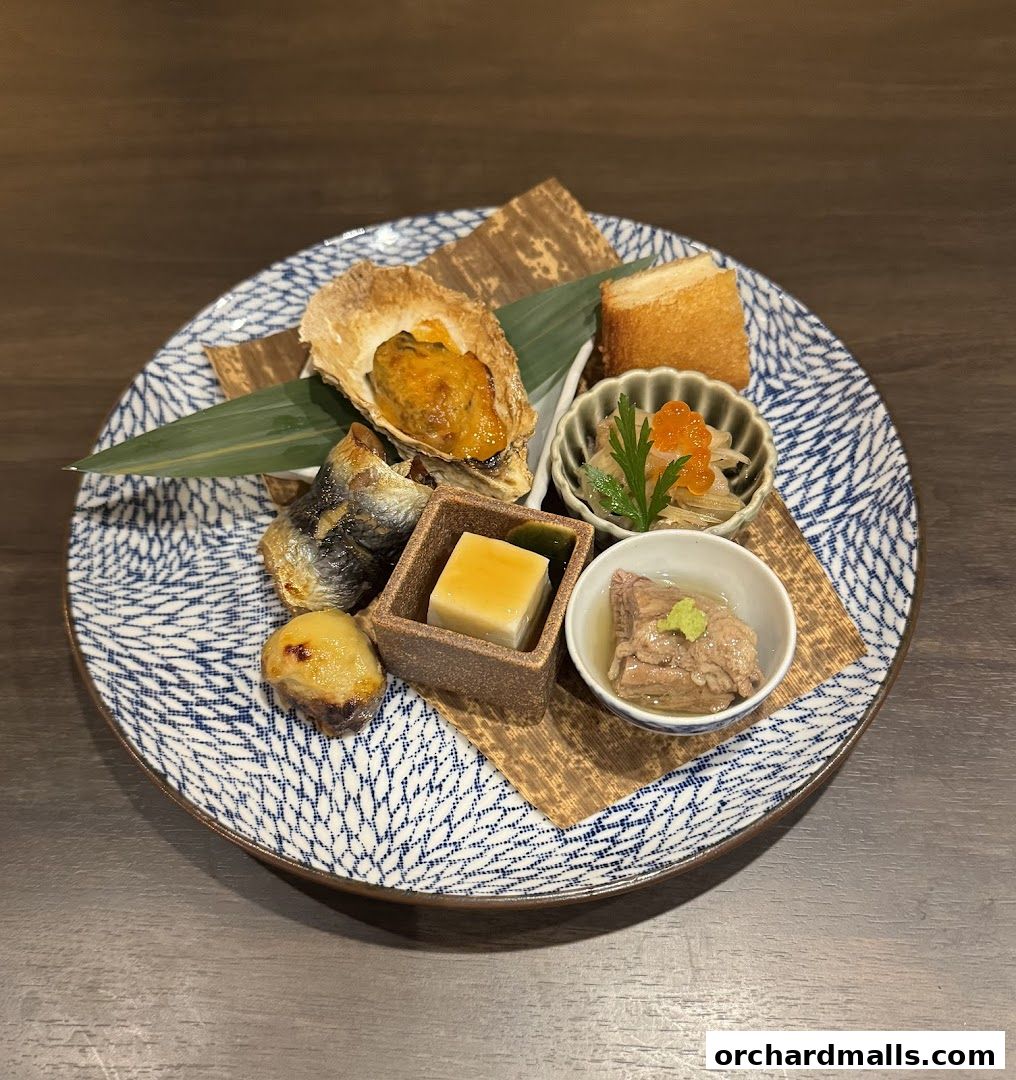 A beautifully arranged plate of assorted Japanese appetizers, including oyster, fish, and tofu.