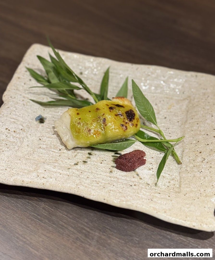 A beautifully plated Japanese dish featuring a piece of fish with a green topping and a small portion of roe.