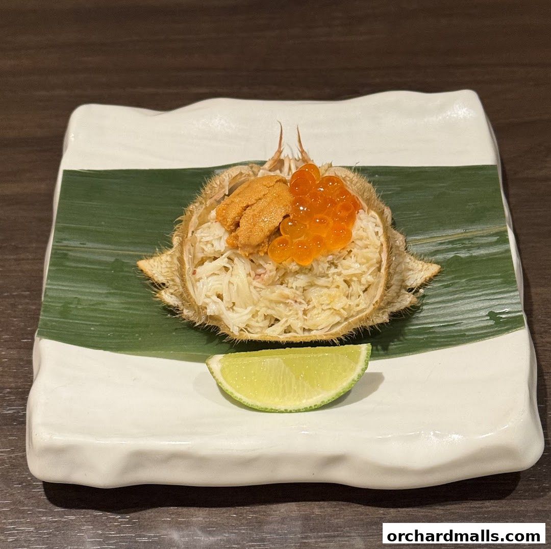 A delicious serving of Japanese cuisine featuring crab, uni, and ikura on a white plate with a lime wedge.