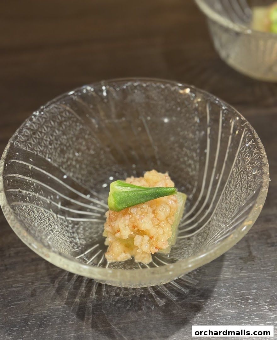 A delicate Japanese appetizer served in a clear glass bowl with a slice of okra.