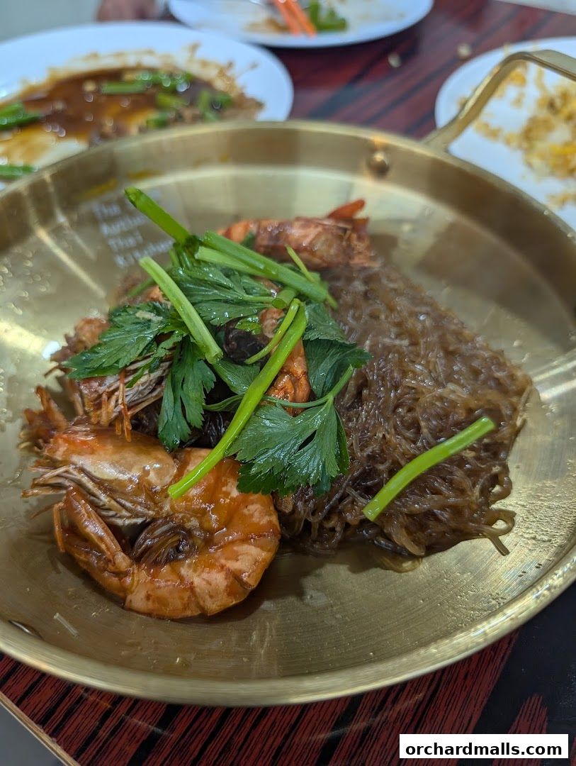 A close-up of a Thai dish featuring prawns and glass noodles served in a brass dish.
