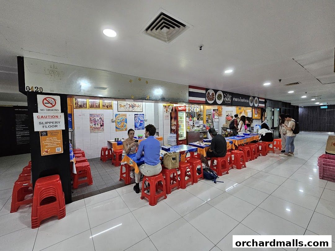 People dining at tables outside a Thai restaurant with red stools and colorful decorations.